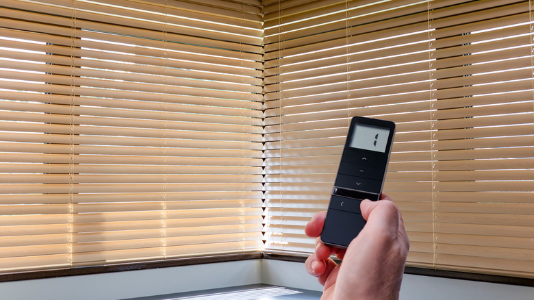 Person controlling automated wooden blinds with remote