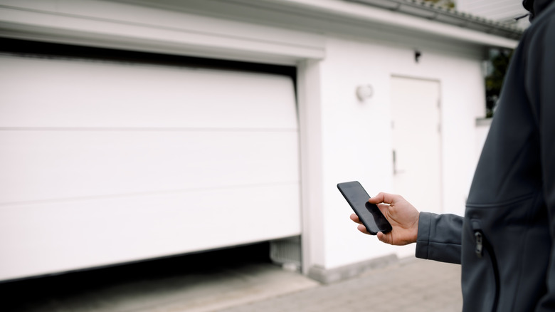 Person holding smartphone and standing in front of half-open garage door