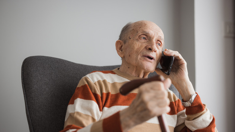 An older adult holding a cane talking on their phone