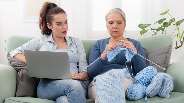 A person on their laptop sitting next to an older person who's knitting