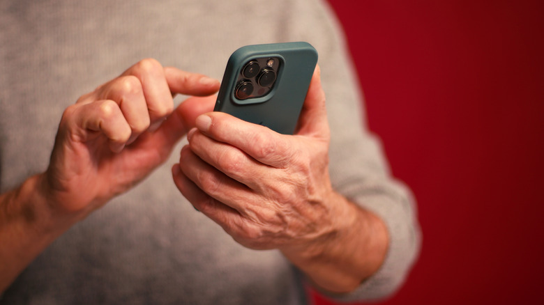 A close-up of an old person using the phone in their hands in front of a red background