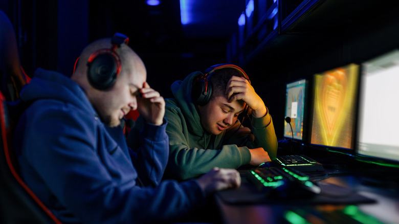Two men in front of computer screens with frustrated expressions and postures.