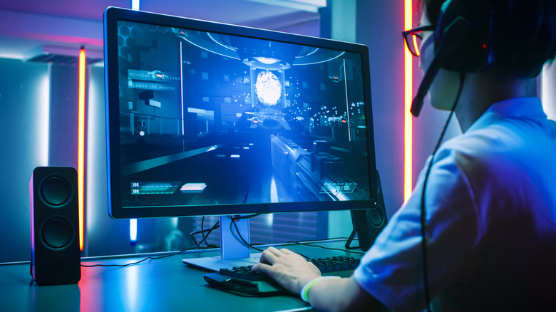 A person plays video games on a PC with a large gaming monitor.