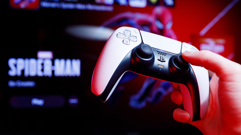 A person hold a PlayStation 5 controller with a slightly blurred Spider-Man image in the background.