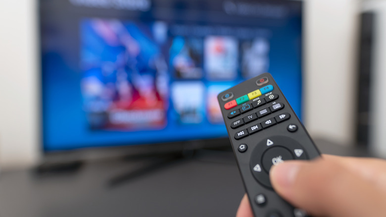A remote with a person changing settings with a blurred TV in the background.