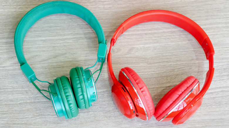 A red pair of headphones next to a green pair of headphones on a wooden table.
