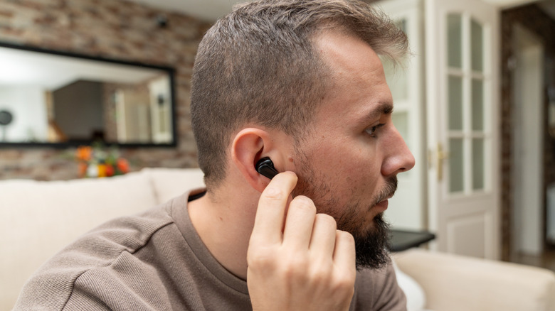 A man removing an earbud from the ear.