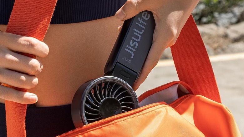 A person slipping the JisuLife Life7 handheld fan into an orange bag.