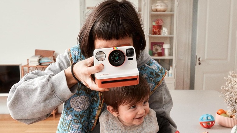 A person using the Polaroid Now 3rd Gen instant camera to take a photo while holding a child.