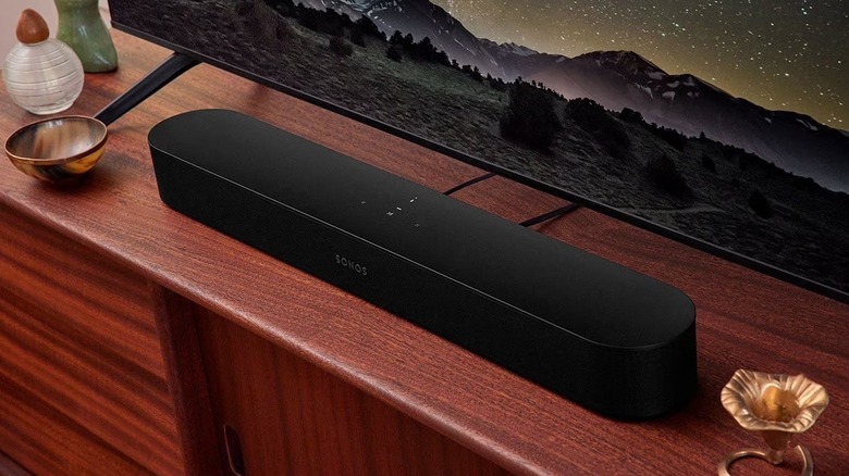 The Sonos Beam Gen 2 soundbar on a wooden surface, in front of a TV.