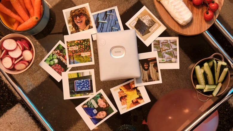 The Fujifilm Instax Square Link photo printer on a glass table, surrounded by photos.