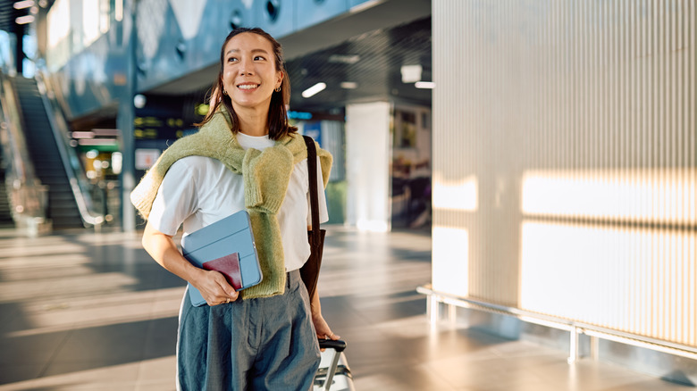 A woman carrying a tablet and passport while walking in an airport.