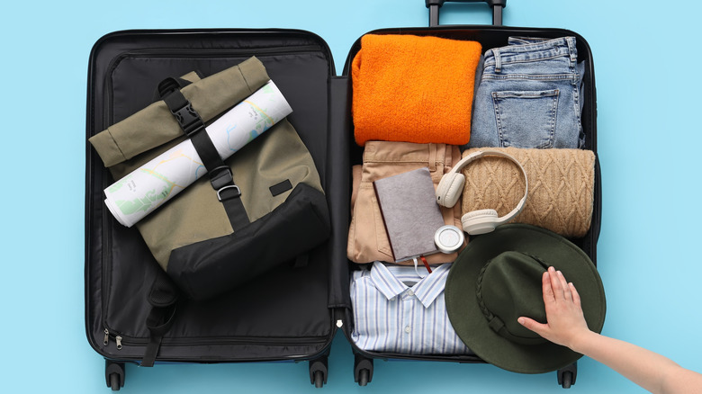 A person packing travel essentials, including headphones, in a suitcase.
