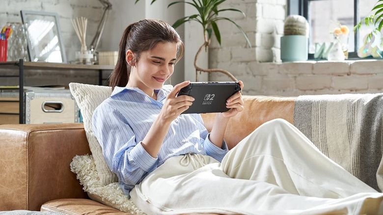 A woman playing the Nintendo Switch 2 gaming console while lounging on a couch.