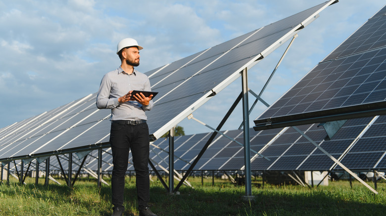 An engineer with a tablet standing outside near several solar panels