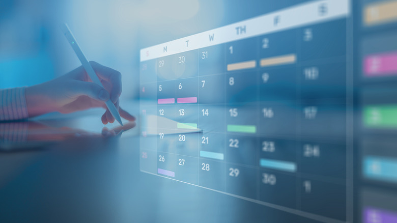 A hand holding a pen next to a digital calendar