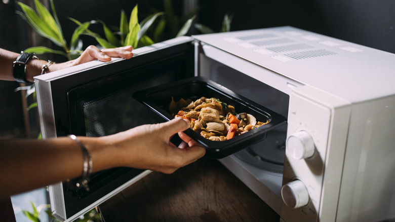 Person placing a plate of food into microwave oven