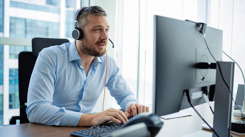 A person in an office working on a computer while wearing a microphone headset.