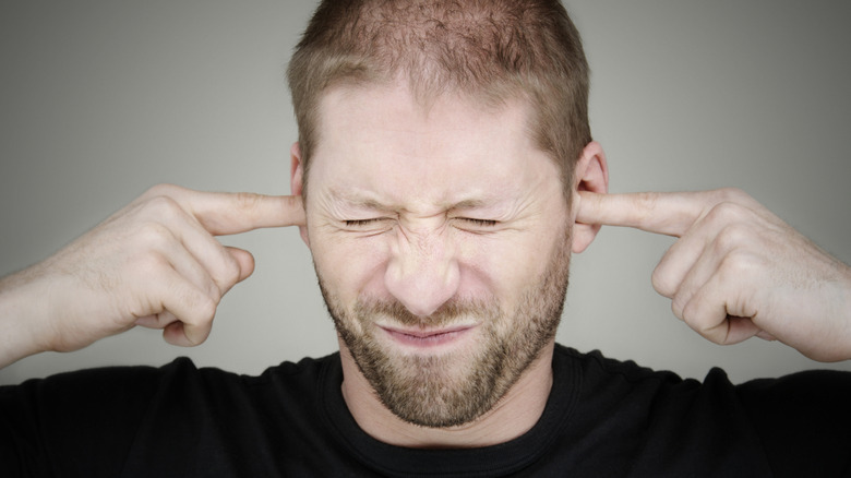 A man grimaces with his fingers in his ears.