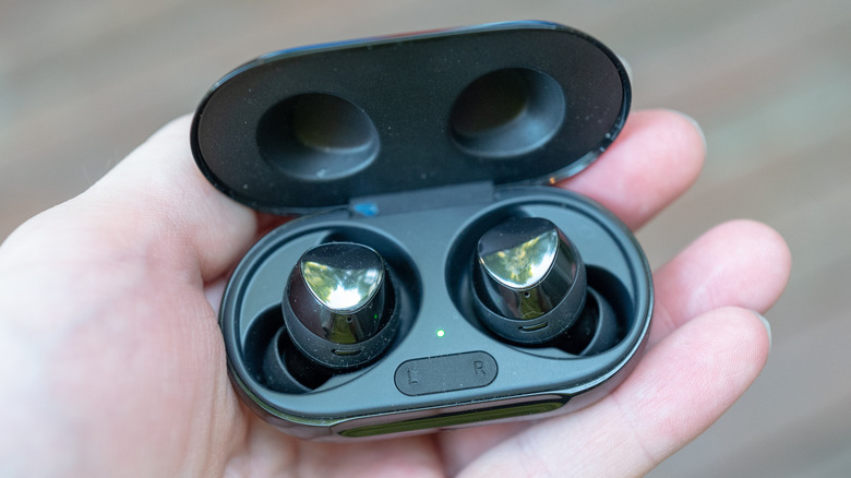 A hand holding an earbud case with two Bluetooth buds inside.