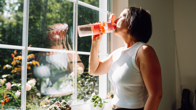 Woman drinking water in front of large window