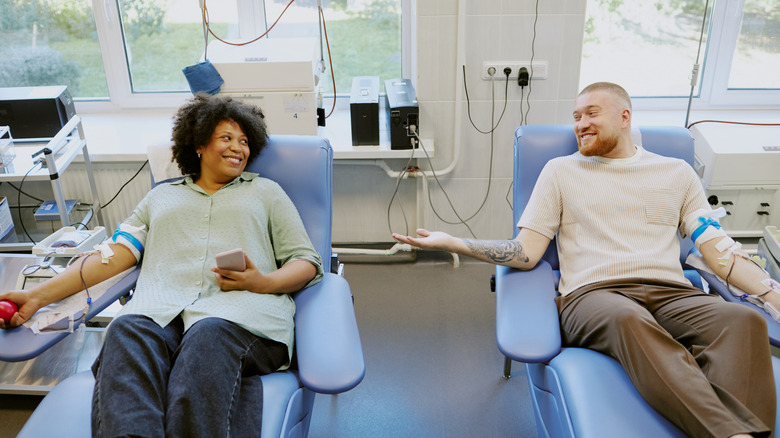 Two individuals sitting in medical chairs donating blood