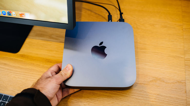 A person holds an Apple Mac Mini in one hand under a computer monitor.