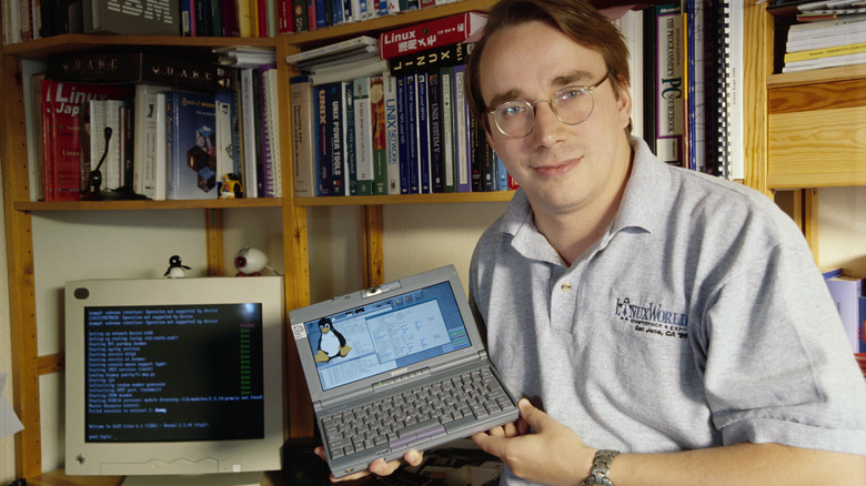 Linus Torvalds holds a small laptop running Linux.