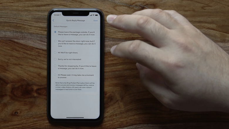 A person's hand next to a phone displaying quick replies on Ring app