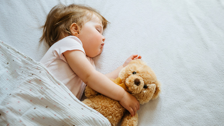 A baby sound asleep holding her teddy bear