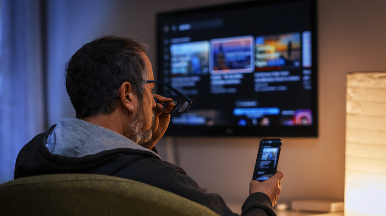 A man distracted by his phone while the T.V. is on