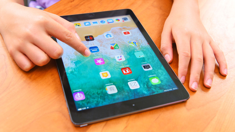 A pair of hands navigating the home screen of an iPad.