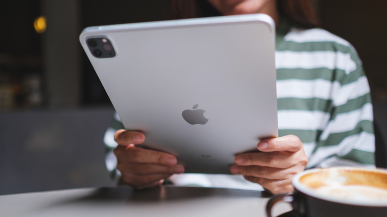 A person holding a silver iPad Pro at a table with a cup of coffee.