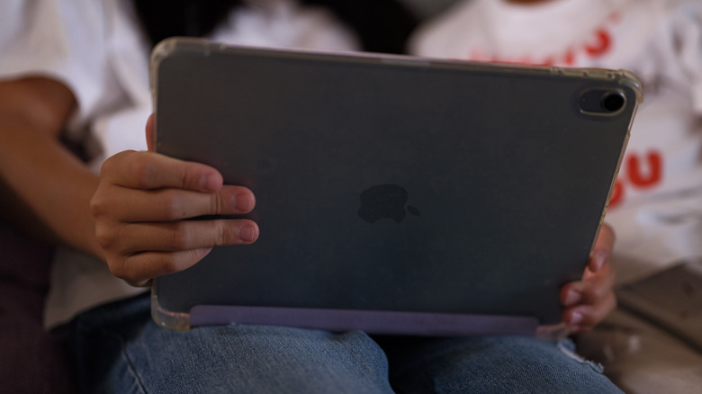 The back of a dark gray iPad facing two blurry seated figures.