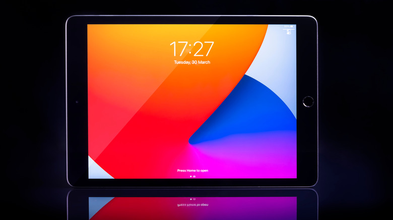 A black 8th-generation iPad displaying the lock screen with one of Apple's default abstract wallpapers.