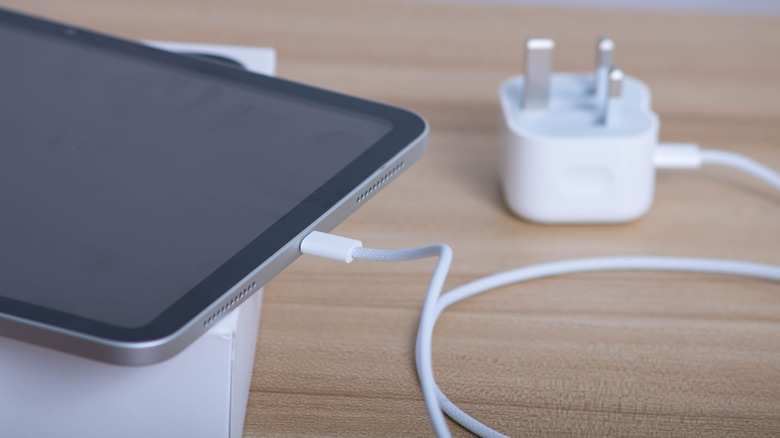 The bottom of an iPad connected to a white Type-C charger with an adapter at the other end of the cable.