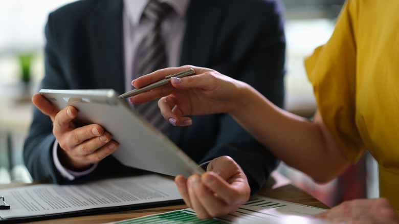 A person in a suit holding an iPad toward someone using a stylus on the device.