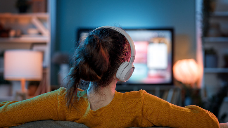 A woman wearing headphones and watching TV.
