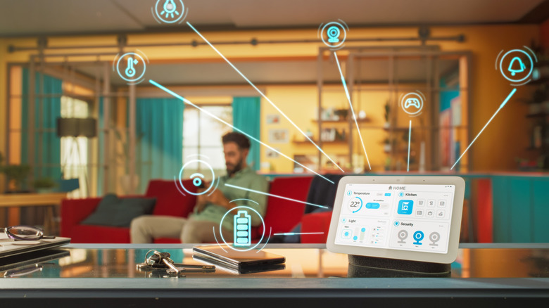 An Amazon Echo Show with icons for smart home devices, on a table with a man in the background.