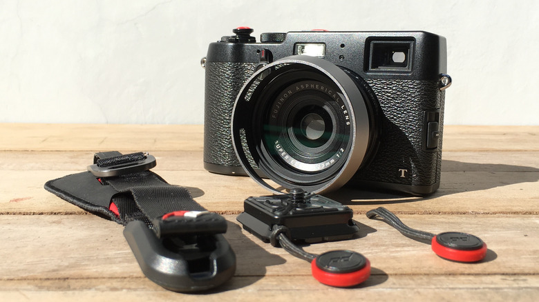A mirrorless camera on a wooden surface alongside a quick-release camera strap system.
