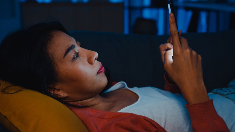 A person lying in bed at night scrolling their phone.