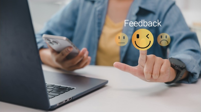Holographic images of feedback emojis beside a laptop and smartphone
