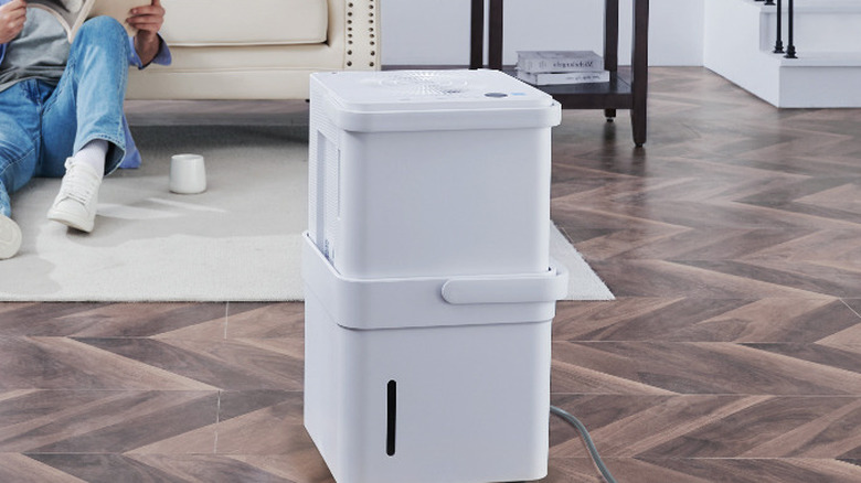 The Midea Cube MAD20S1QWT dehumidifier in the living room, while a person reads a magazine in the background.