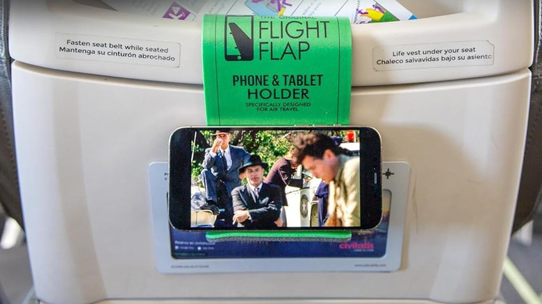 A green Flight Flap Phone Holder supporting a phone hooked to a back seat panel.