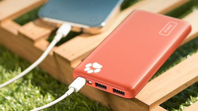 A red Iniu B41 power bank with a white charging cable plugged in, placed outdoors on a pallet.