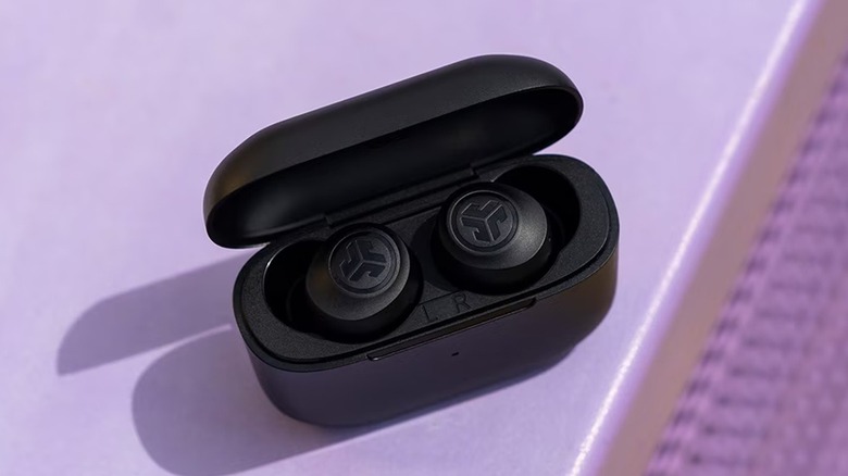 Black JLab Go Air Pop wireless earbuds in their charging case on a lilac surface.