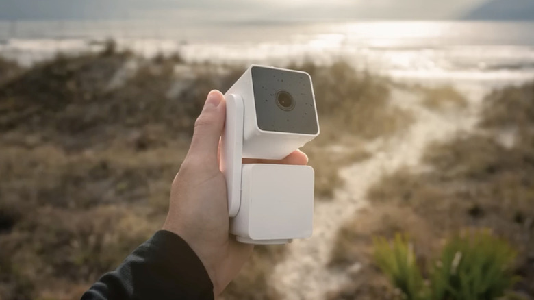 The Wyze Cam Pan V3 security camera in someone's hand against a blurred landscape background.