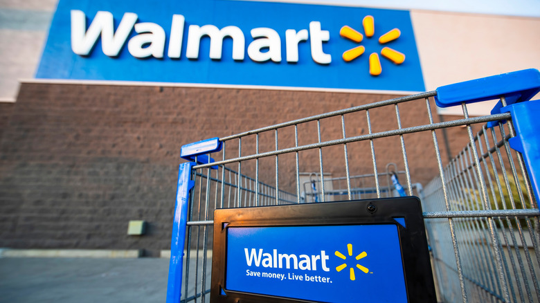 A Walmart-branded shopping cart in front of a physical store with the Walmart logo at the top.