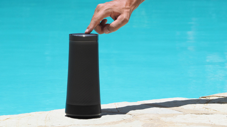 A portable speaker next to a pool, with a hand tapping it.