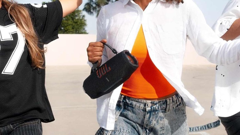 The JBL Charge 6, held by its carry strap, in a woman's hand.